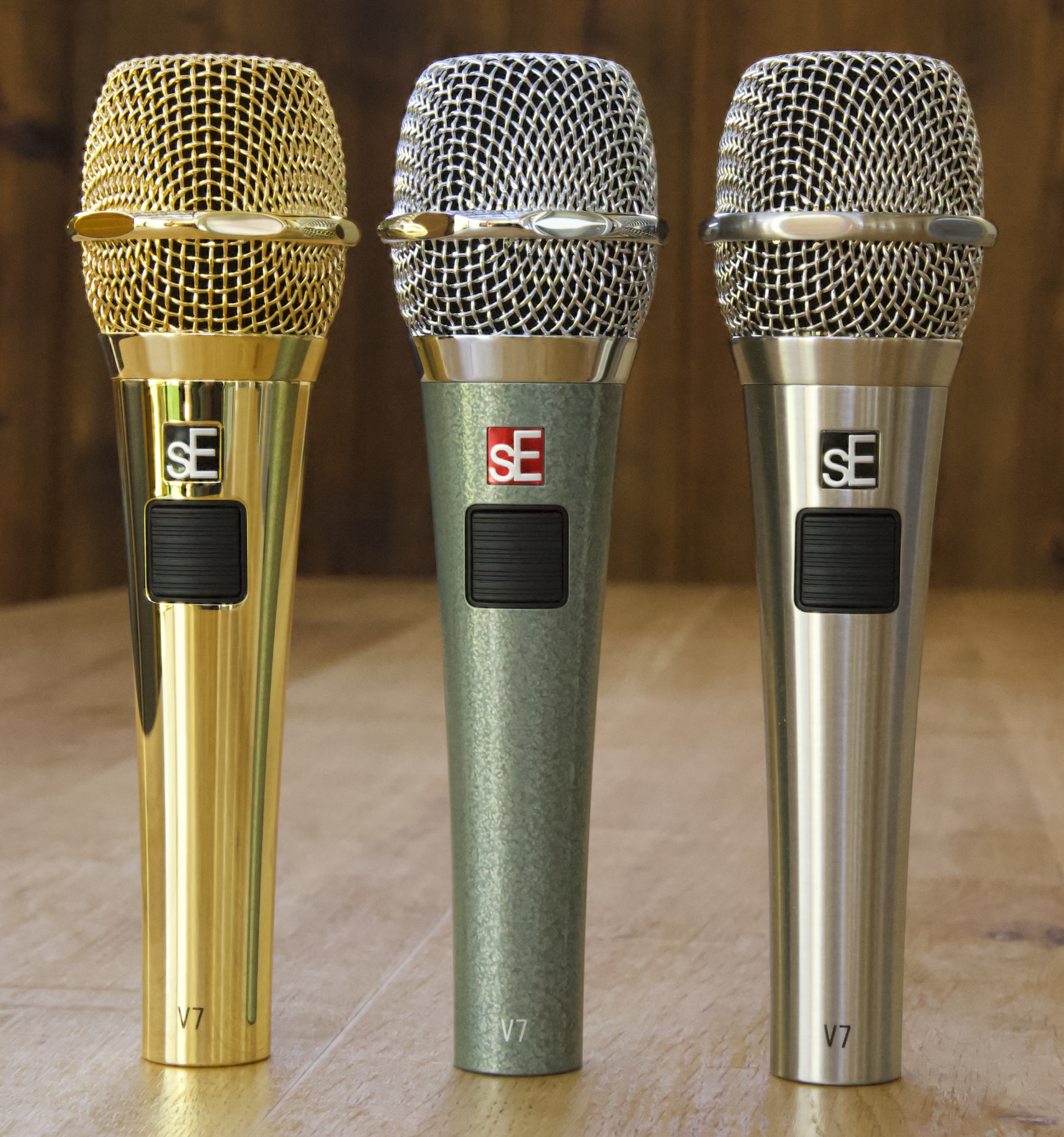 sE Electronics V7 PTT in Gold, Vintage Edition, and Brushed Nickel standing on a wood background.